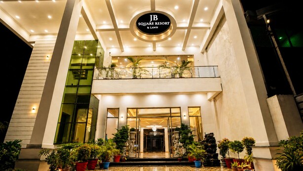 A hotel entrance with a sign reading 'JB Square Resort & Lawson,' featuring a modern design with a glass facade, a balcony with plants, and a tiled entrance area. - Hotel JB Square Ayodhya Near Ram Mandir, Airport & Ayodhya Cantt (Faizabad)