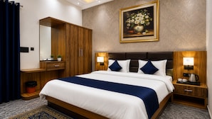A hotel room with a large bed, a wooden wardrobe, a bedside table with a lamp, and a painting on the wall. - Hotel JB Square Ayodhya Near Ram Mandir, Airport & Ayodhya Cantt (Faizabad)