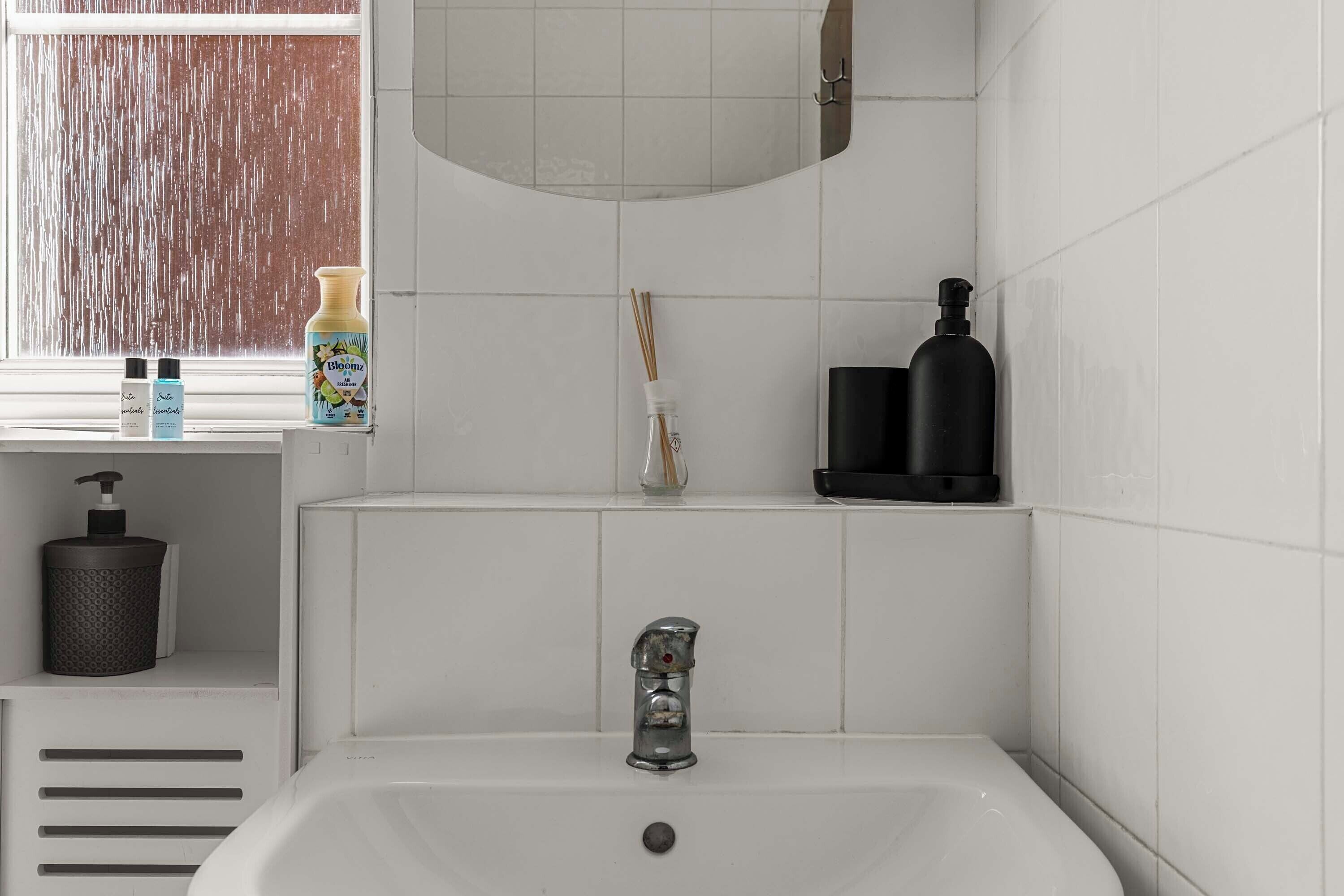 A bathroom with a white sink, a mirror, and a window with a view of a wooden structure.
