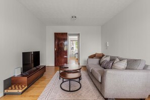 A living room with a TV, sofa, coffee table, and a door leading to another room. - Modern 2BR SW19 | Ideal for Long Stays & Professionals (London)