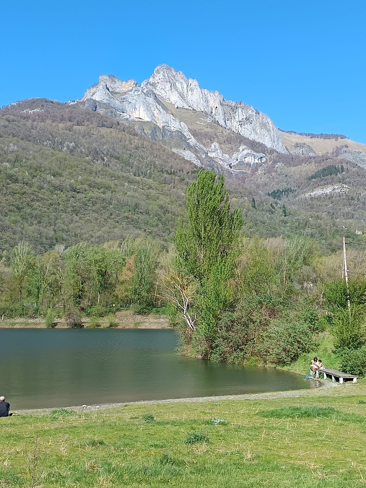 A lake with mountains in the background, a grassy area, and a bench.