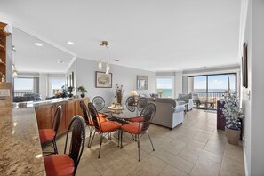 Een ruime woonkamer met een eettafel, stoelen en een balkon met uitzicht op zee.