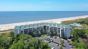 Ein mehrstöckiges Hotel mit Blick auf den Strand, inklusive Parkplatz und Poolbereich.