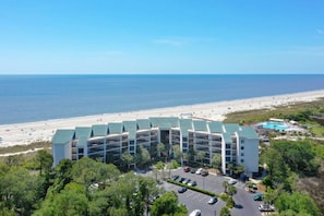 Un hotel de varios pisos con vista al mar, estacionamiento y zona de piscina.