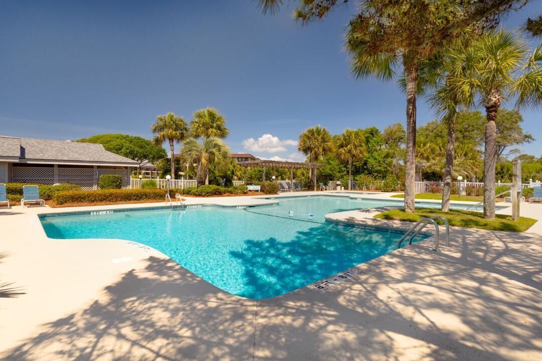 Une piscine à l’eau d’un bleu cristallin, entourée de palmiers et avec un bâtiment visible au loin.