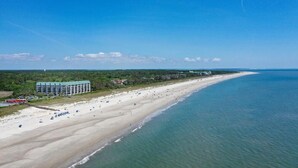 A coastal hotel with a long beachfront, a large building with a green roof, and a sandy beach with umbrellas. - New! Gorgeous Oceanfront 208 Sea Cloisters 2 BR Pool Beach Bikes and Beach Gear (Hilton Head Island)
