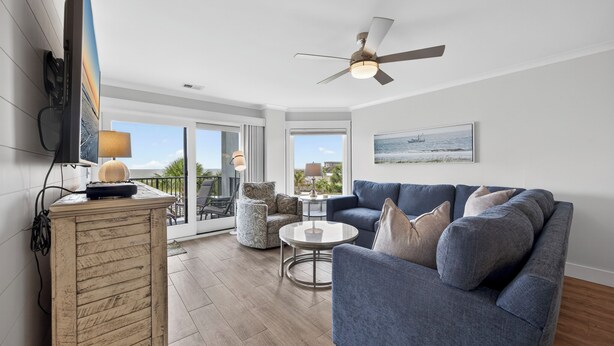 A spacious living area with a blue sofa, a round coffee table, and a ceiling fan. - New! Gorgeous Oceanfront 208 Sea Cloisters 2 BR Pool Beach Bikes and Beach Gear (Hilton Head Island)
