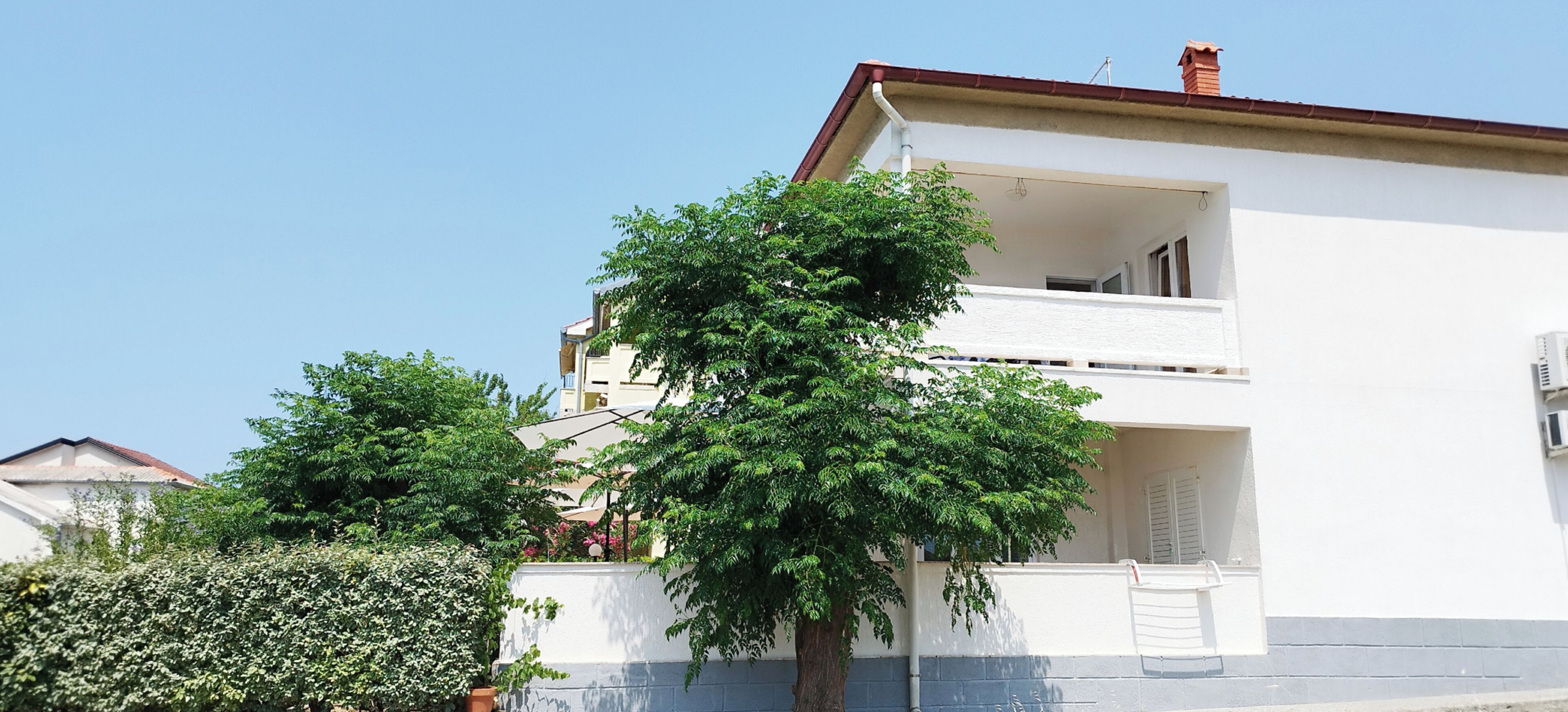 A two-story building with a balcony, a tree in front, and a clear sky.