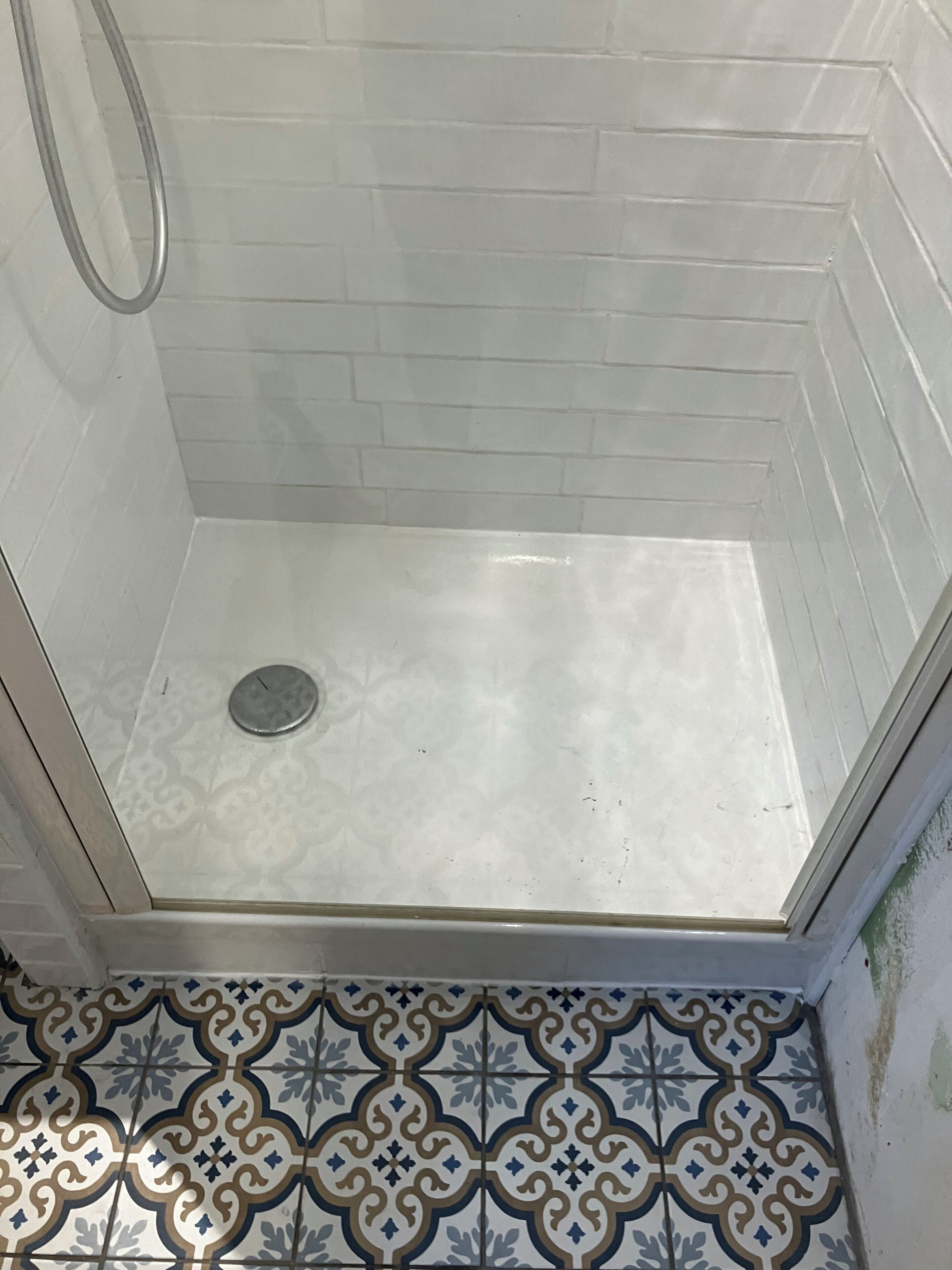 A shower with a white tiled wall and a patterned floor.
