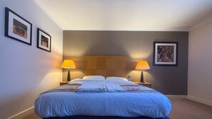 Une chambre d’hôtel avec un grand lit, deux lampes de chevet, une tête de lit en bois et des œuvres d’art encadrées accrochées aux murs.