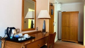 Une chambre d’hôtel avec un bureau en bois, deux lampes, un miroir, une armoire et un plateau avec des tasses et une bouilloire.