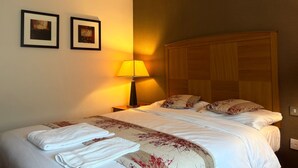 Une chambre d’hôtel avec un lit, deux tableaux encadrés au mur, une lampe et une tête de lit en bois.
