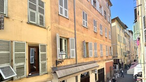 A narrow street lined with multi-story buildings, some with shutters, and a few people walking. - Espace Barillerie 12 - Old Town (Nice)