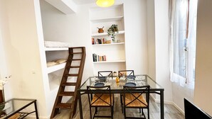 A room with bunk beds, a ladder, a glass table with chairs, a bookshelf, and a window with curtains. - Espace Barillerie 12 - Old Town (Nice)