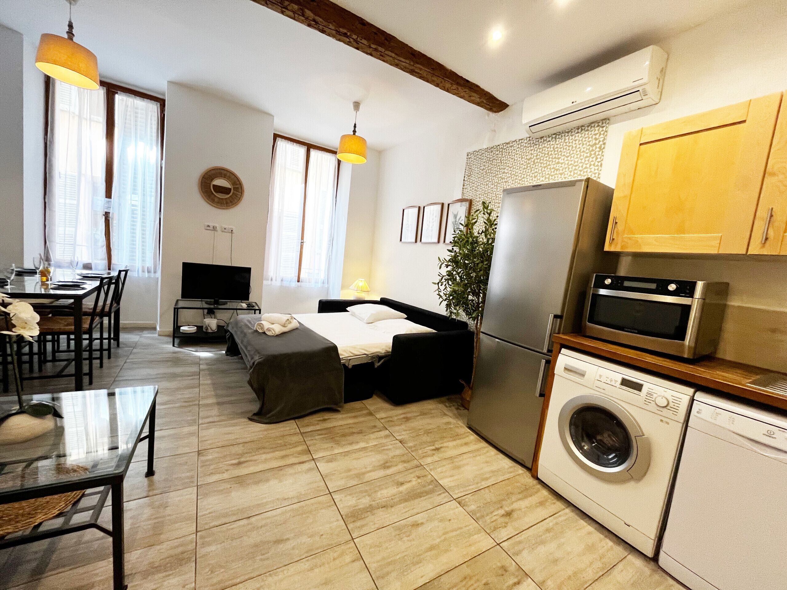 Une chambre d’hôtel compacte comprenant un lit, un coin repas avec une table et des chaises, un téléviseur, un lave-linge et un appareil de climatisation.
