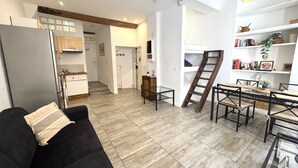 A modern living room with a black sofa, a glass coffee table, and a wooden ladder. - Espace Barillerie 12 - Old Town (Nice)