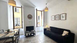 A living room with a black sofa, a dining table with chairs, and a TV on a stand. - Espace Barillerie 12 - Old Town (Nice)