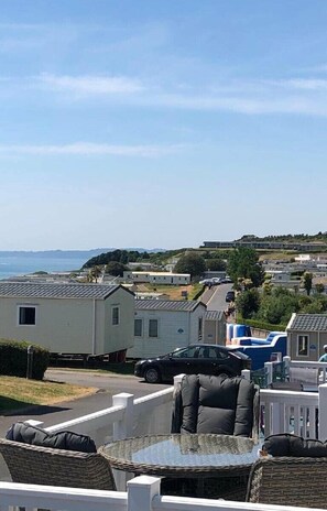A view of a coastal area with mobile homes, a car, and a wicker table with cushions. - Devon Cliffs Holiday Park - Holiday Accommodation 12845 (Exmouth)