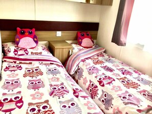 Ein Doppelbett mit zarter Bettdecke mit Blumen- und Eule-Motiv, einem Holz-Kopfschild und einem Nachttisch mit Lampe.