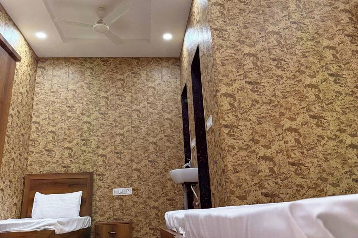 Une chambre à coucher avec deux lits en bois, un ventilateur de plafond, un éclairage encastré et un papier peint à motifs.