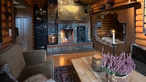 A cozy log cabin interior with a stone fireplace, wooden furniture, and a dog.