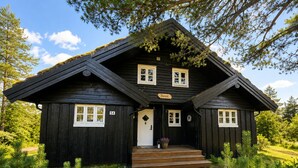 A black wooden cabin with a stone pathway leading to the entrance, surrounded by greenery.