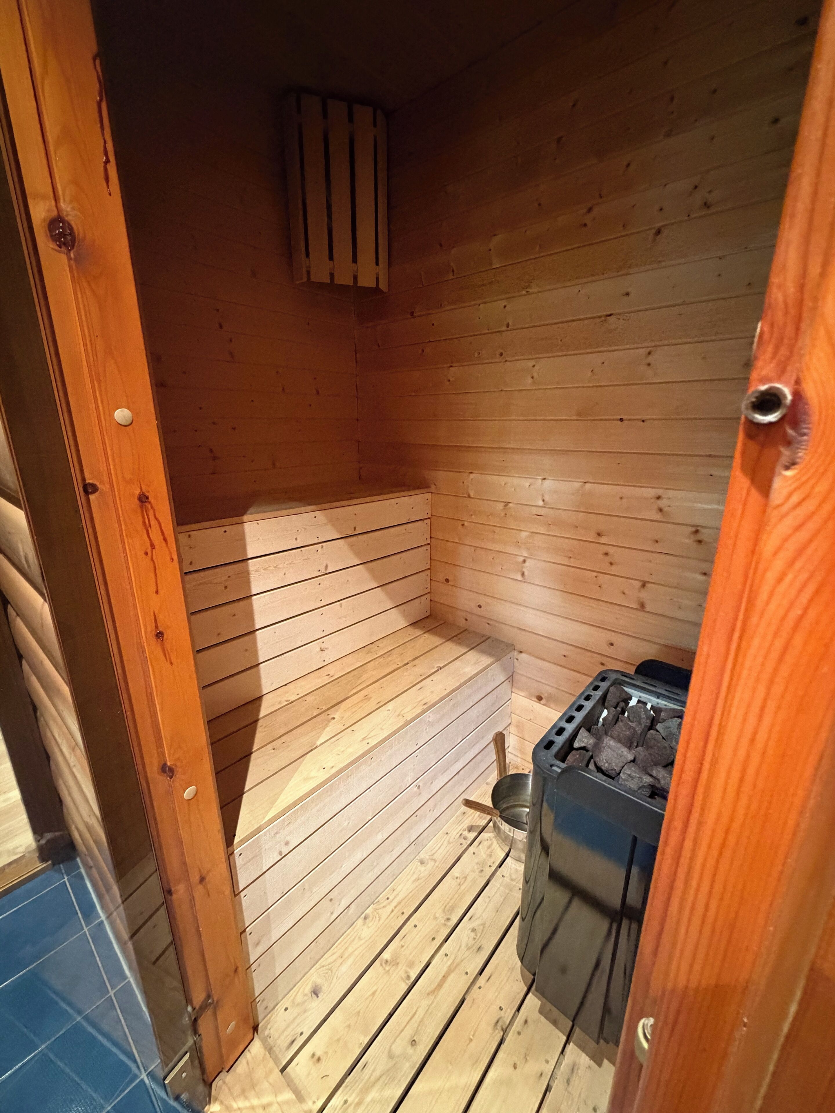 Un sauna en bois, avec un banc, un seau et un appareil de chauffage.