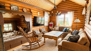 A log cabin interior with a living room, sofa, rocking chair, and a television.