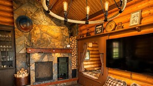 A cozy log cabin interior with a fireplace, seating area, and a television.