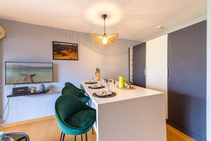 A modern kitchen with a central island, green chairs, a hanging light fixture, and a framed picture on the wall. - Charmant studio au bord du lac avec sa terrasse et sa vue sur les montagnes (Duingt)