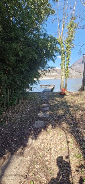 A pathway leading to a dock by a lake, surrounded by trees and vegetation. - Charmant studio au bord du lac avec sa terrasse et sa vue sur les montagnes (Duingt)