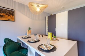 A modern dining area with a white table, green chairs, a hanging light fixture, and a painting on the wall. - Charmant studio au bord du lac avec sa terrasse et sa vue sur les montagnes (Duingt)
