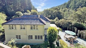 A two-story building with a sloped roof, surrounded by dense forest. - Amazing 4bedroom dog/family friendly lodge with hottub/fire bowl in Cornish wood (Bodmin)