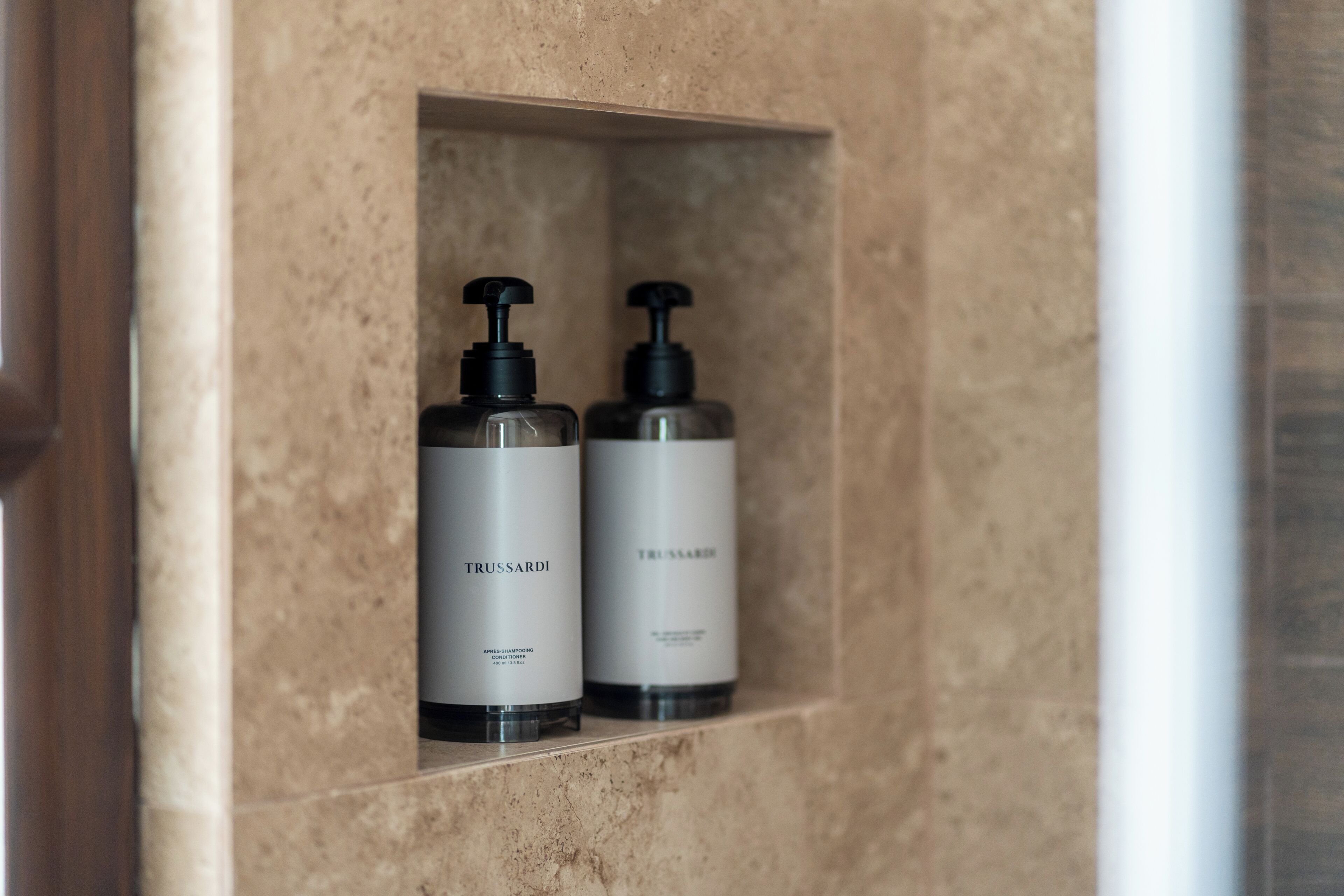 Two bottles of Trussardi shampoo and conditioner in a bathroom shelf.