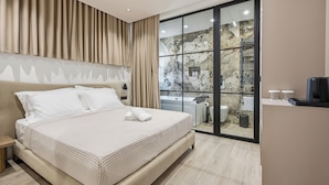 Une chambre moderne avec un grand lit, une porte-fenêtre coulissante donnant sur une salle de bain et une vue sur un mur en pierre.