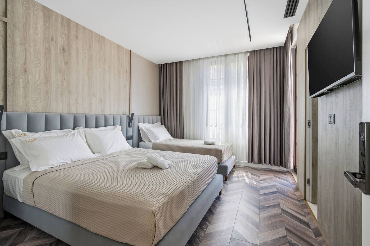 Quarto de hotel com uma cama grande, uma cama menor, uma televisão e uma parede de madeira.