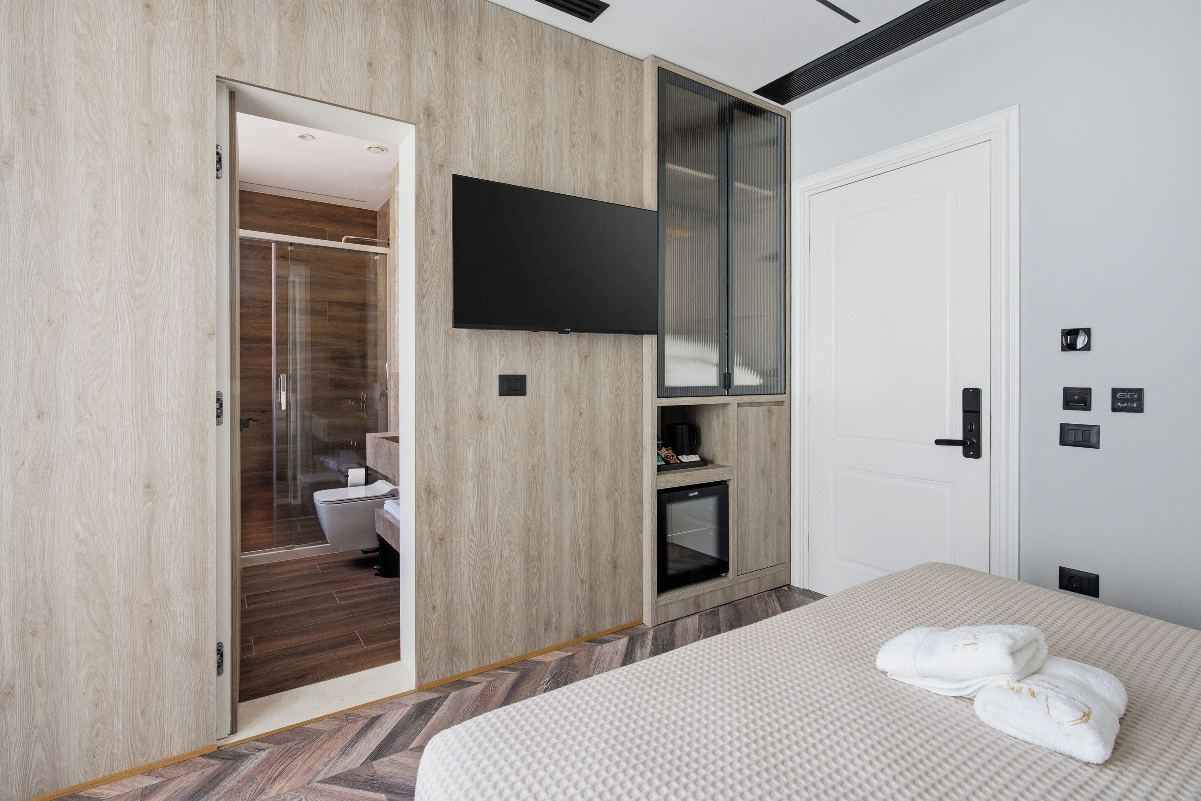 Quarto de hotel moderno com uma cama, televisão na parede, guarda-roupa e uma pequena cozinha.