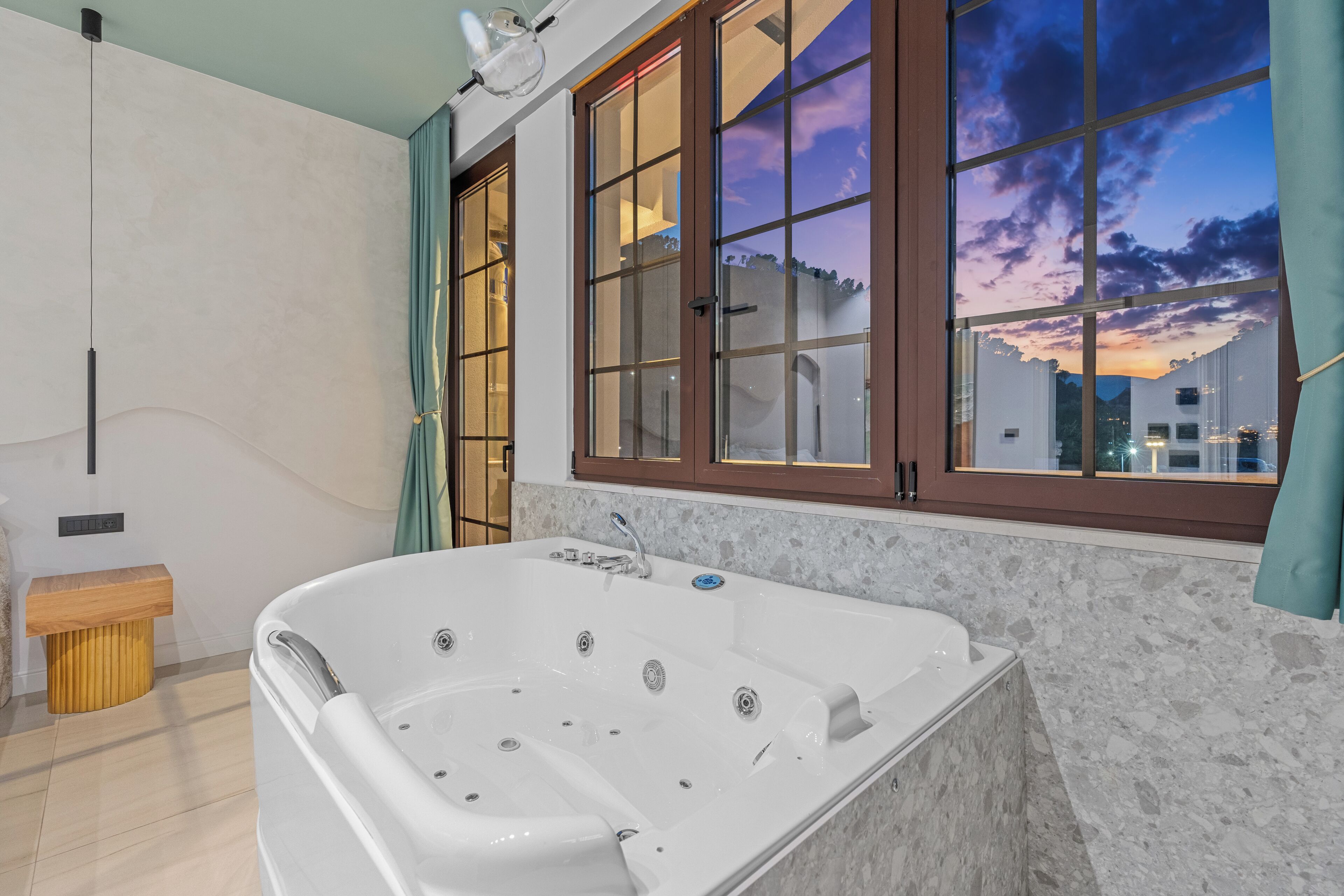 Une salle de bain moderne avec une grande baignoire, un banc en bois et une vue sur le paysage urbain grâce à de grandes fenêtres.