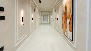 Un long couloir étroit doté d’un plancher poli, de luminaires fixés aux murs et d’un grand tableau abstrait accroché au mur de droite.