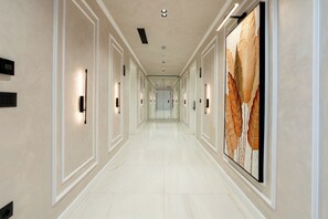 A long, narrow hallway with a polished floor, wall-mounted light fixtures, and a large abstract painting on the right wall. - Art Boutique Hotel Berat (Berat)