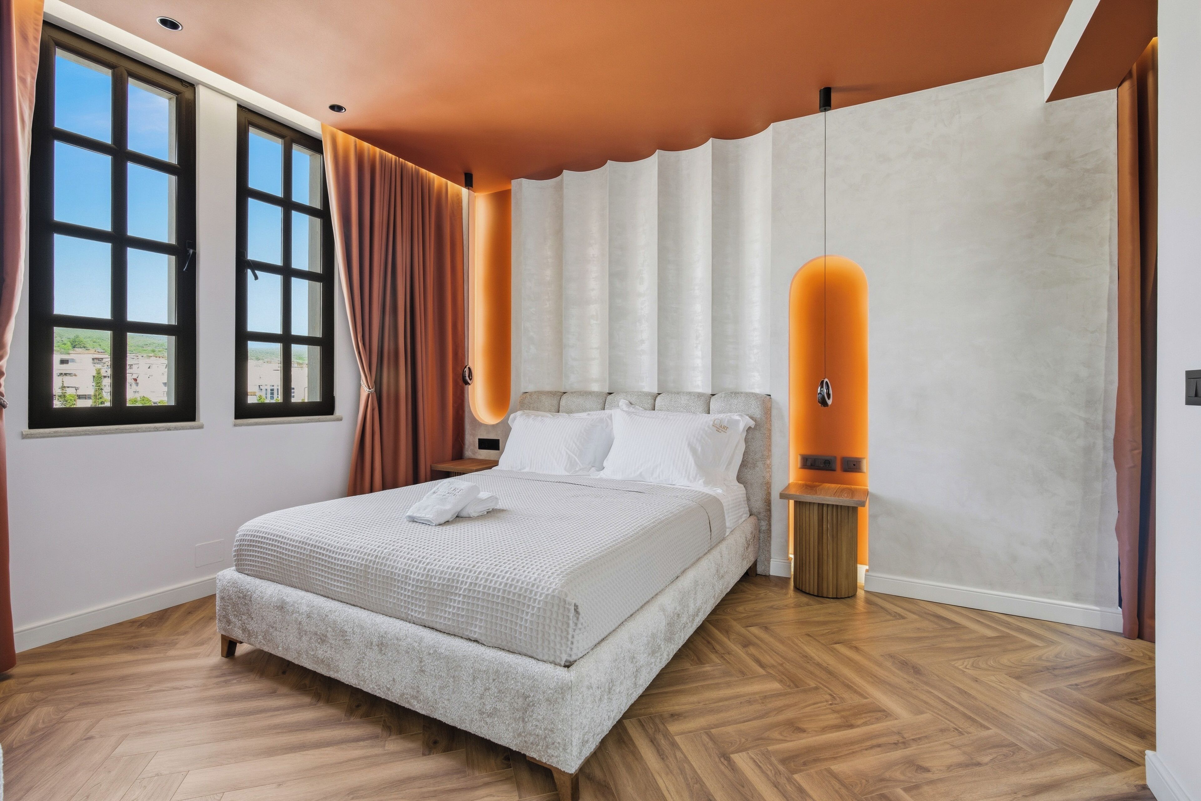 A modern bedroom with a large bed, a nightstand, a wall-mounted lamp, and a window with curtains.