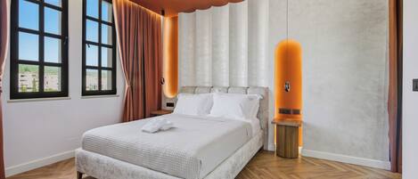 A modern bedroom with a large bed, a nightstand, a wall-mounted lamp, and a window with curtains.