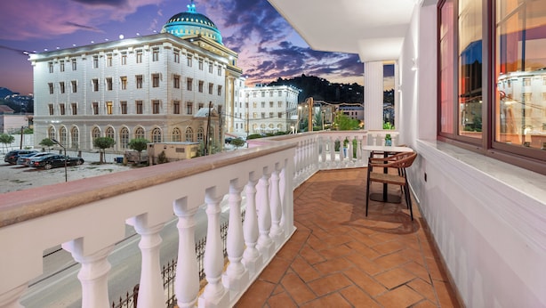 Un balcon doté d’une balustrade blanche, d’une chaise et offrant une vue sur un grand bâtiment surmonté d’un dôme.