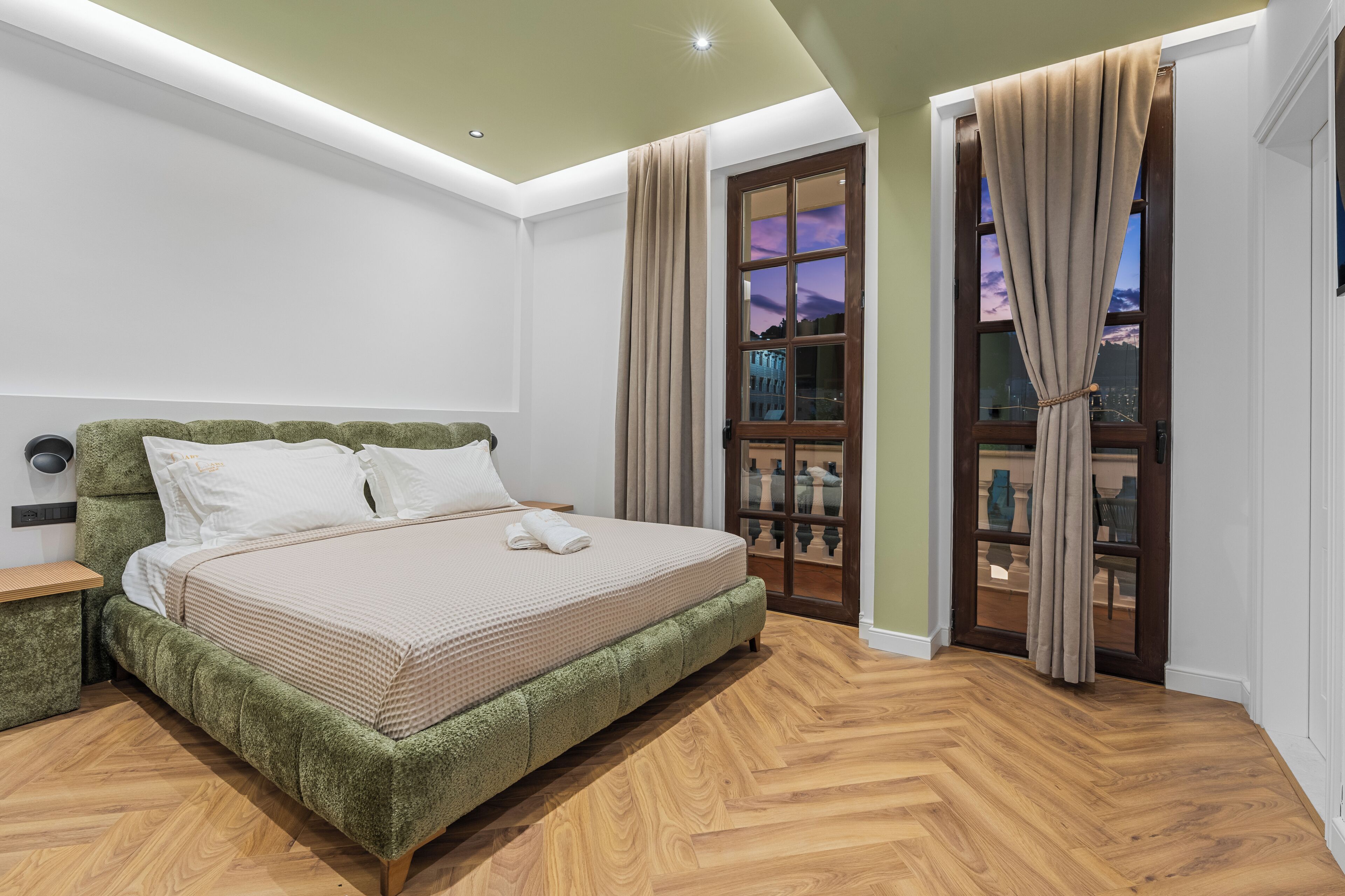 Een slaapkamer met een bed, houten vloeren, een raam met gordijnen en een deur.