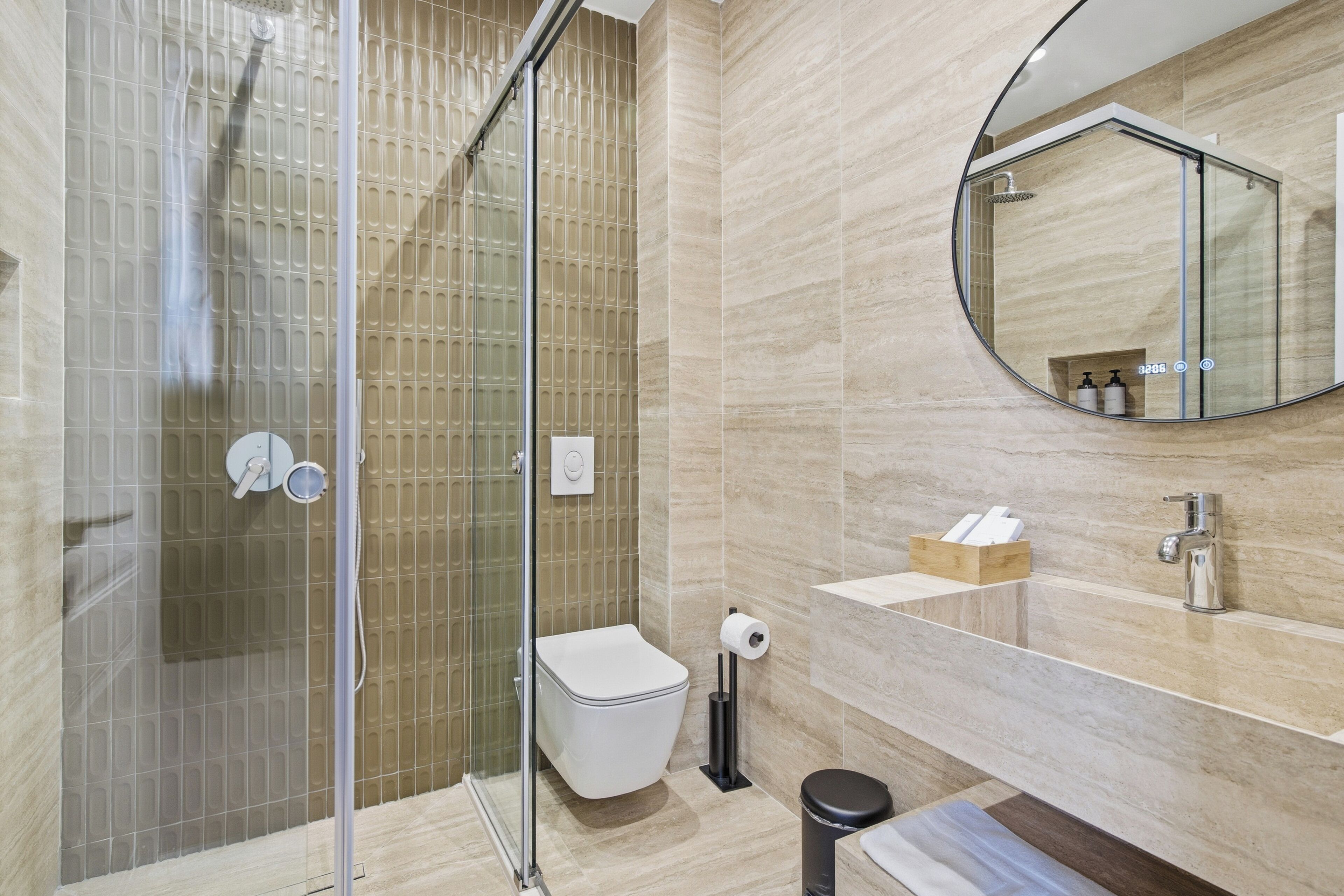 Une salle de bain moderne avec une douche à parois de verre, des toilettes, un lavabo avec un miroir et une poubelle.