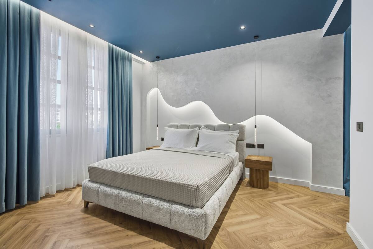 Quarto moderno com cama, mesas de cabeceira e uma cabeceira com design ondulado.