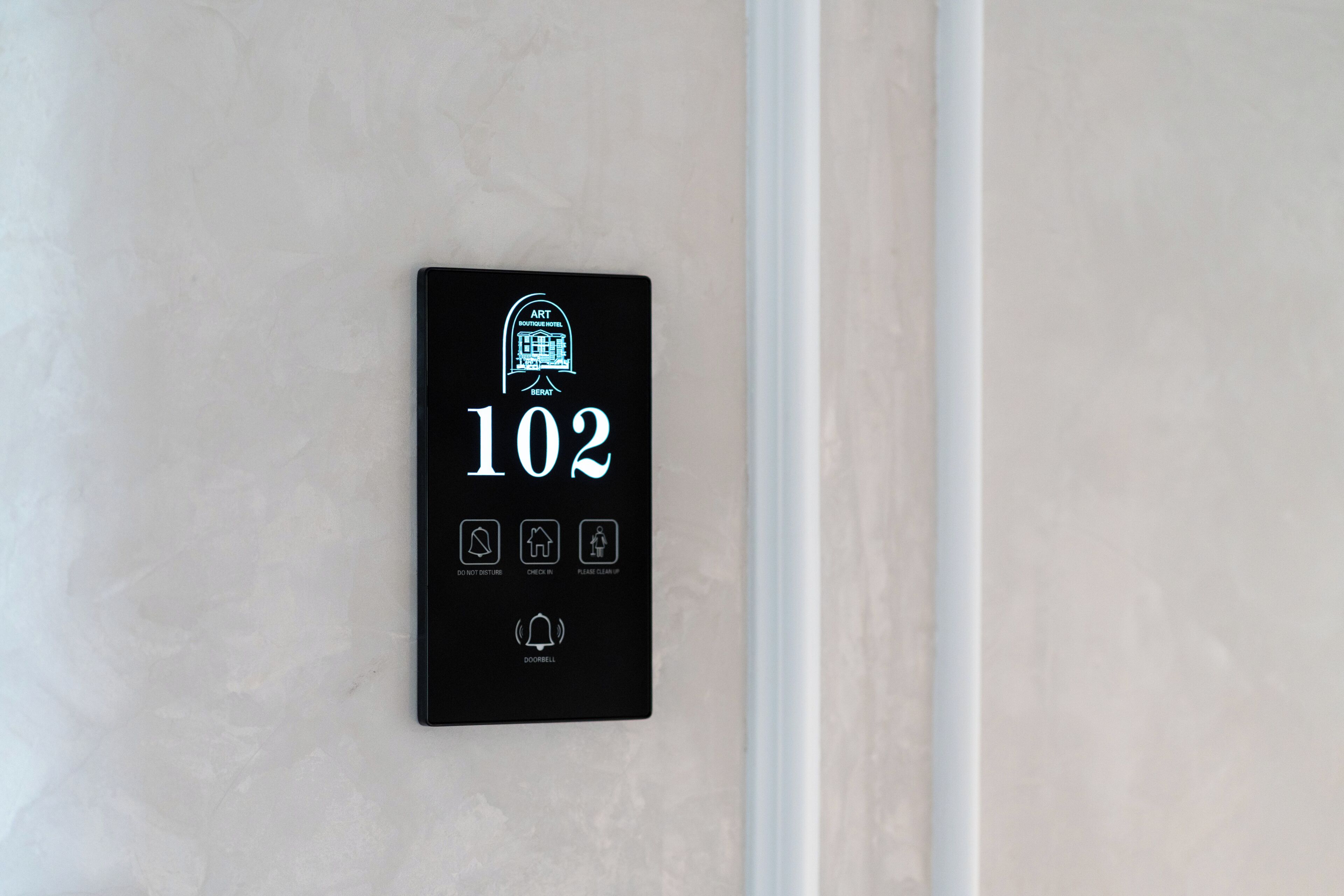 Un panneau noir fixé au mur, portant le numéro 102 (numéro de la chambre), ainsi que des icônes indiquant la présence d’un concierge, d’un service d’enregistrement et d’un service de nettoyage.