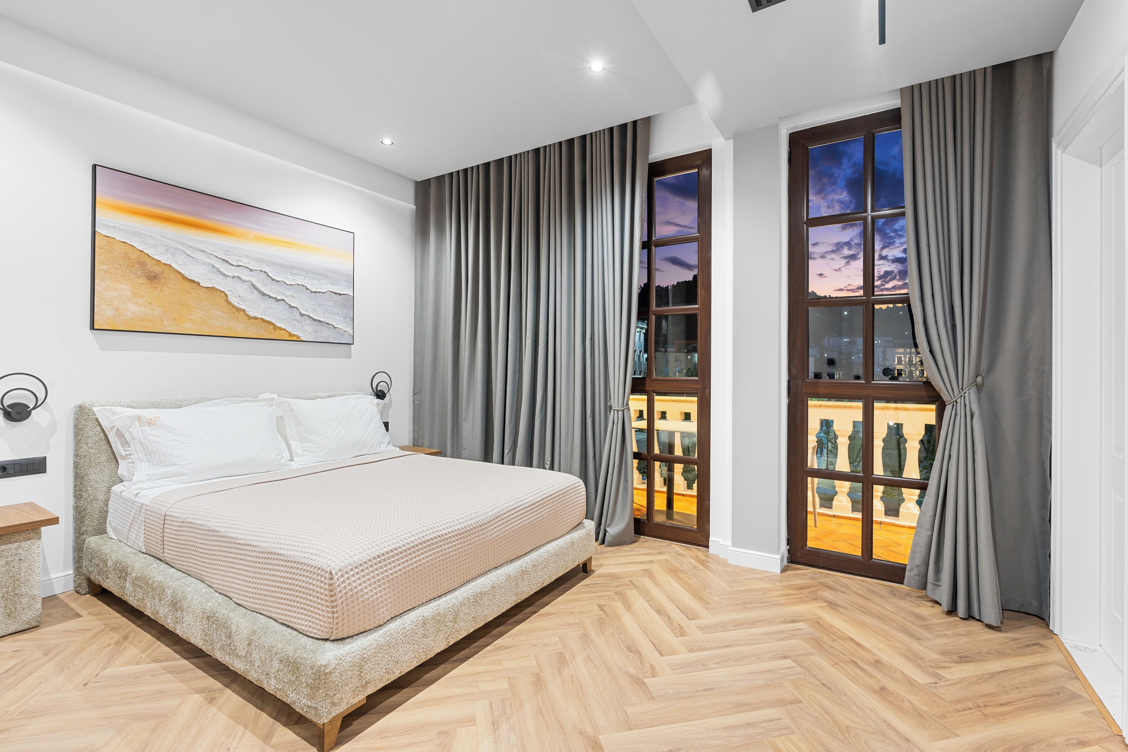 A bedroom with a bed, a painting, a window with curtains, and a view of the city.