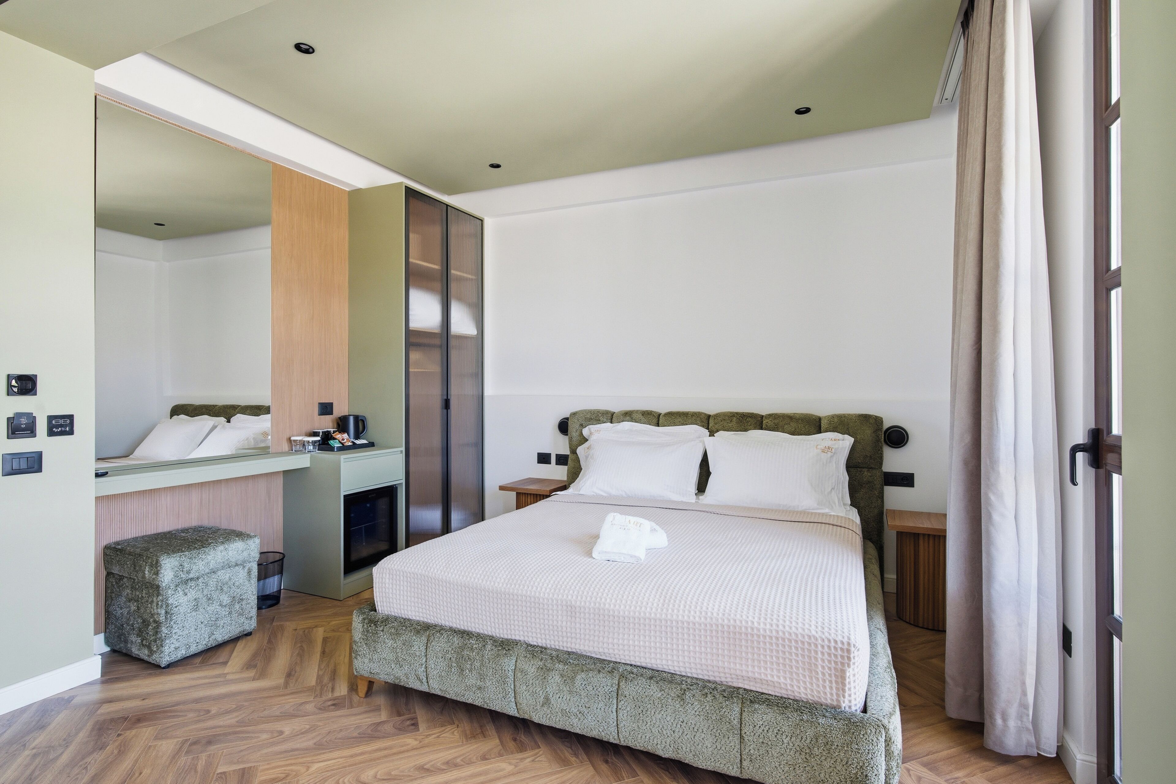 A hotel room with a bed, a small desk, a mirror, a wardrobe, and a wooden floor.