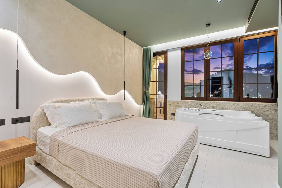 Quarto moderno com uma cama grande, uma banheira e vista para a cidade pela janela.